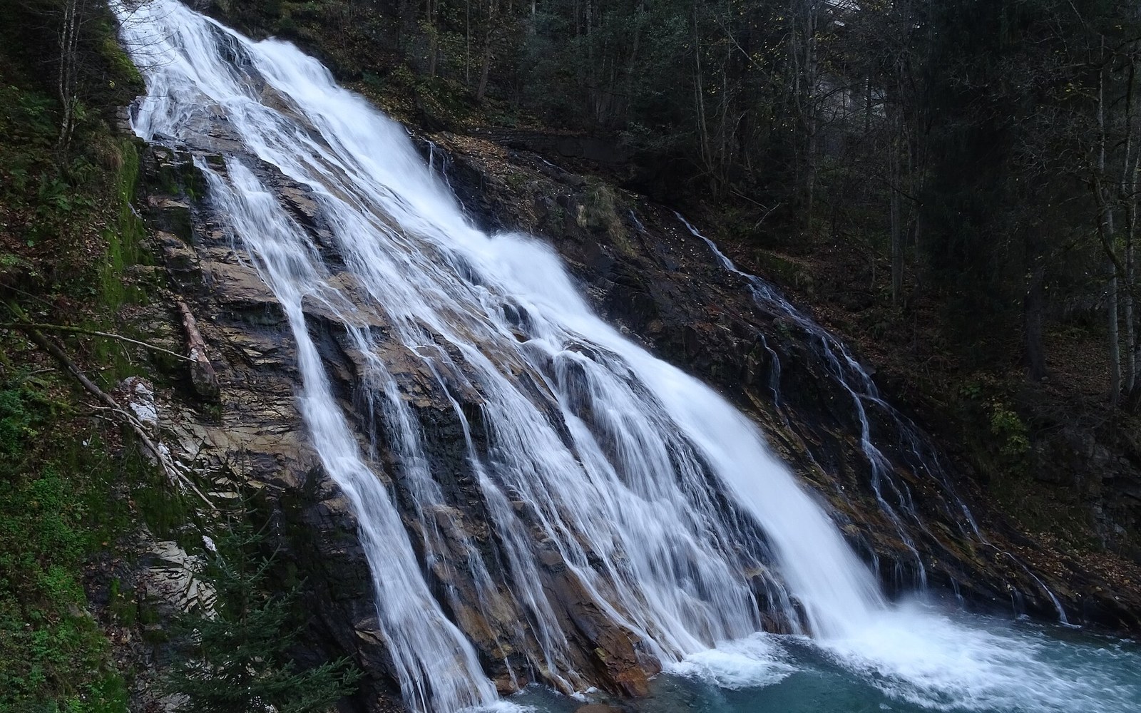 Waterfall cascading down a rocky cliff into a pool surrounded by forest