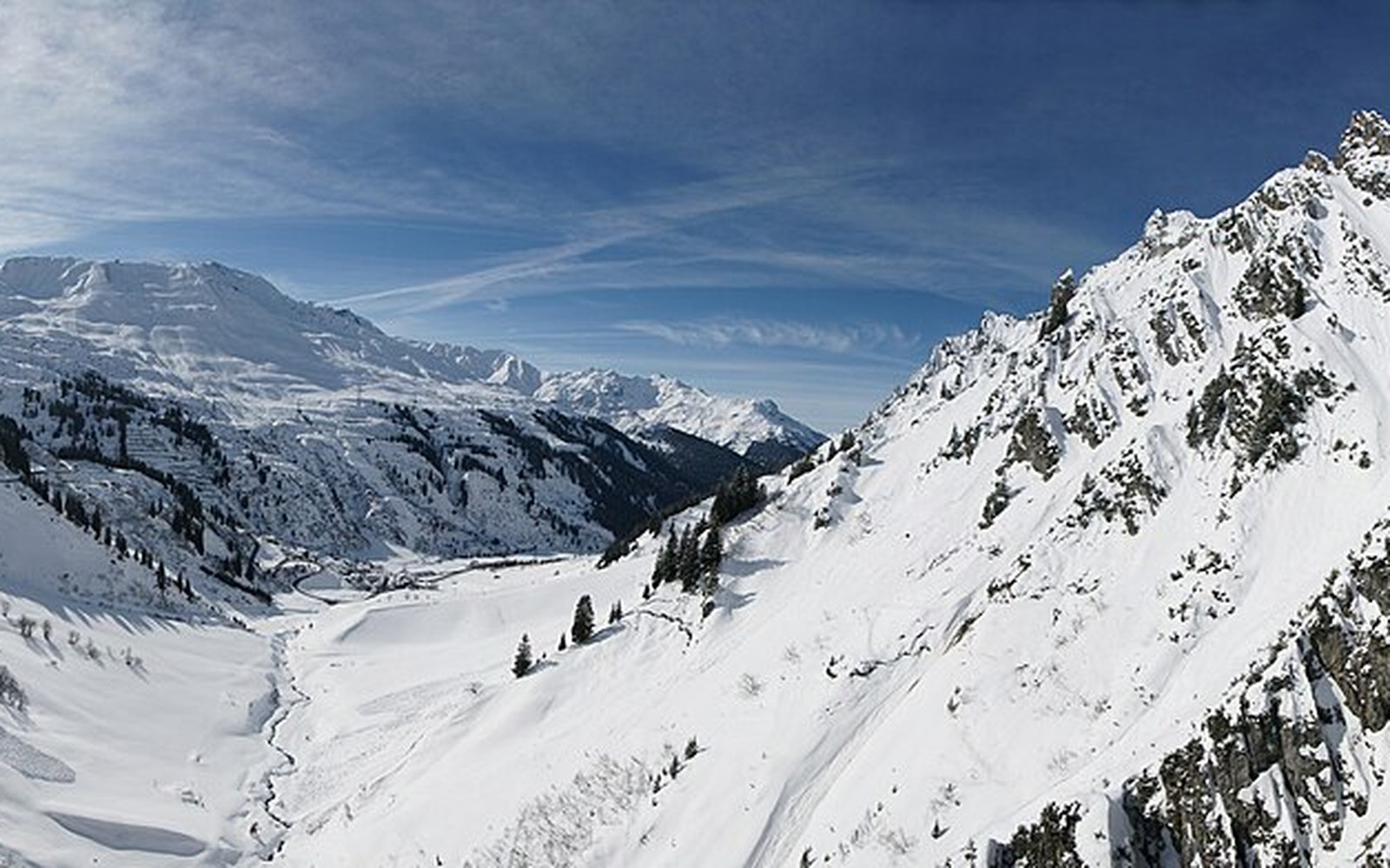 Snow-covered alpine valley with jagged peaks flanking a village nestled below