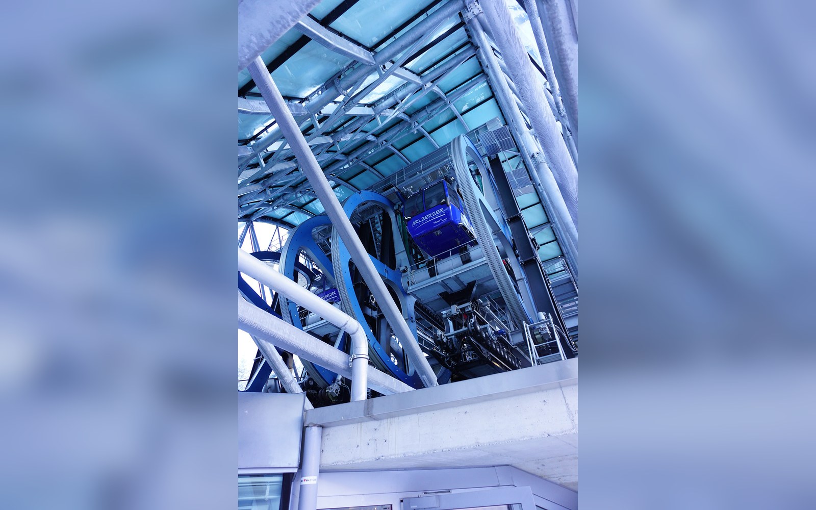Large blue cable car wheel mechanism inside the Galzigbahn station's glass-roofed structure