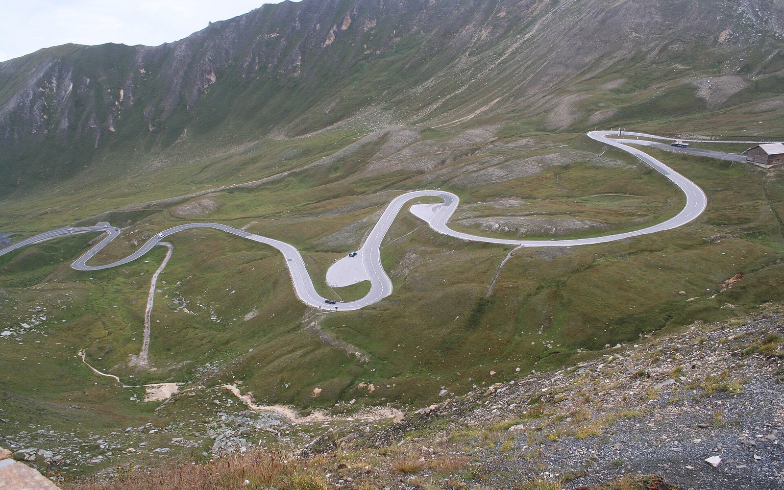 A hairpin road cut into a high alpine slope with a glacier valley beyond